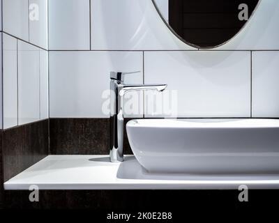 Moderno rubinetto in acciaio inox su lavabo in ceramica bianca nel bagno con specchio. Lavabo in ceramica a forma rettangolare pulito su decori in marmo Foto Stock