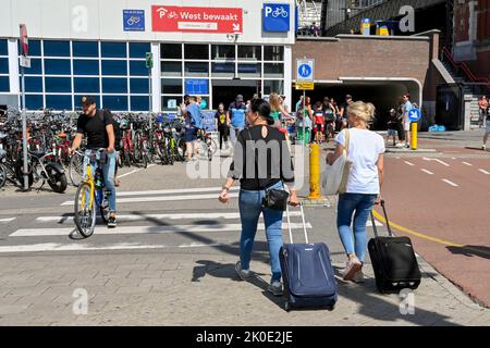 Amsterdam, Paesi Bassi - 2022 agosto: Due persone che tirano valigie a piedi fino alla stazione ferroviaria principale della città Foto Stock