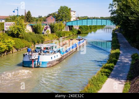 Una chiatta motorizzata carica di ghiaia naviga su un canale attraverso un'area urbana in una giornata estiva di sole. Foto Stock