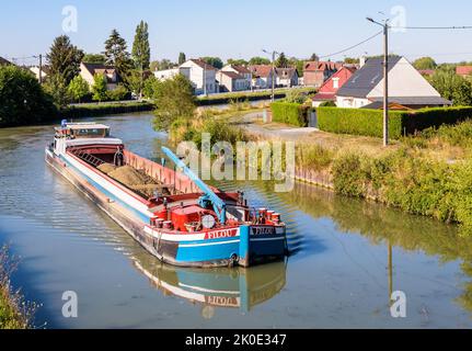 Una chiatta motorizzata carica di ghiaia sta navigando su un canale attraverso un'area urbana in una mattinata estiva soleggiata. Foto Stock