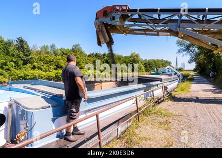 Un bargeman sta guardando il carico con la ghiaia della sua chiatta motorizzata ormeggiata su un canale in una cava di sabbia in una giornata di sole estate. Foto Stock