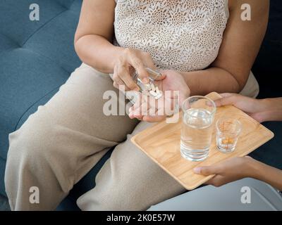 Primo piano delle mani di donna anziana tiene la pillola e un bicchiere di acqua potabile da figlia giovane adulta, preso la medicina quotidiana o integratori vitaminici, elderl Foto Stock