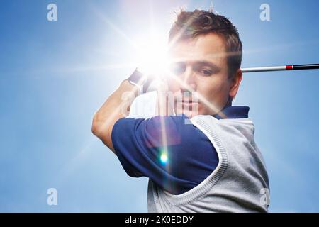 HES si è concentrato sul suo swing. Giovane uomo in piena oscillazione durante una partita di golf contro un cielo blu. Foto Stock