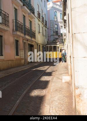 Lisbona, Portogallo, 24 ottobre 2021: Vista della ripida e stretta strada di Lisbona con la tipica linea gialla vintage del tram numero 28, icona e simbolo del Foto Stock