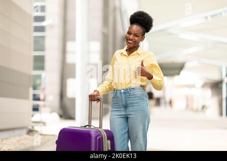Allegro Nero Tourist Woman gesturing Thumbs Up posa in aeroporto Foto Stock