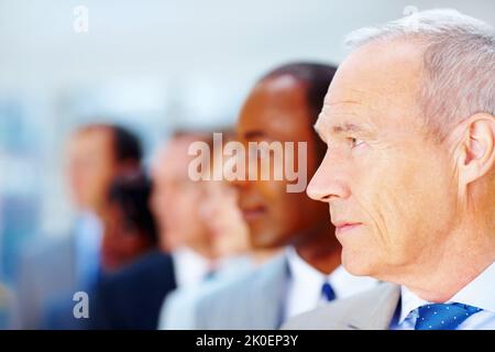 Dirigente senior serio con team in background. Vista laterale di un uomo d'affari senior con il team dietro di lui. Foto Stock