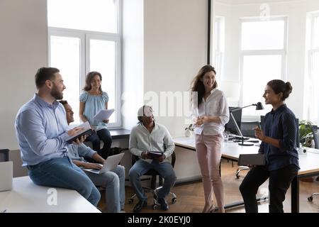 Felice dipendente indiano che condivide idee con i colleghi durante il briefing Foto Stock