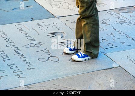 Un giovane ragazzo taglia i piedi sulle impronte di famose star del cinema nel cortile anteriore del Graumans Chinese Theater di Hollywood Foto Stock