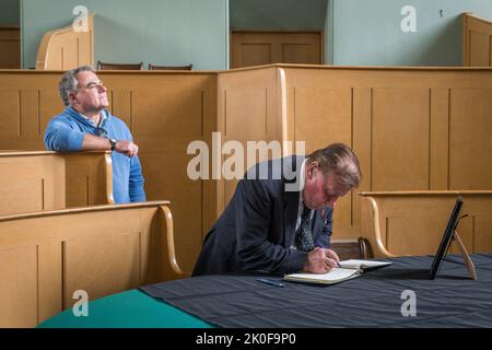 Nella piccola città di confine gallese di Presteigne, la vecchia città della contea di Radnorshire, l'agricoltore Brian Lloyd firma un libro di condoglianze per la defunto Regina Elisabetta II Il libro è conservato nella vecchia corte del Giudice's Lodging, nel centro della città. Foto Stock