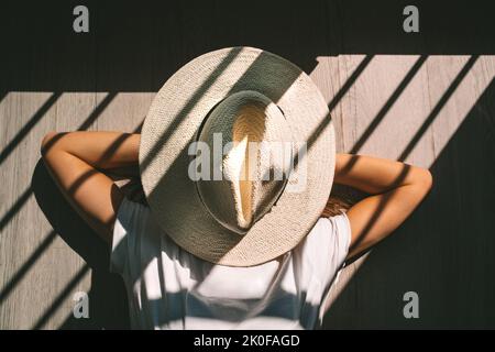 Giovane donna con cappello in testa che si posa a terra al tramonto. Donna che si gode del tempo libero e pigro fine settimana. Foto Stock