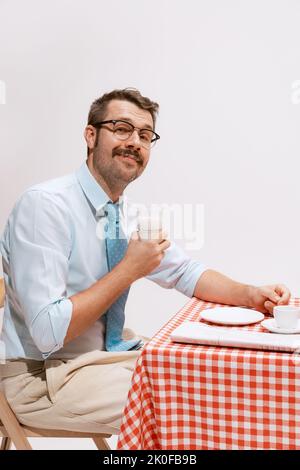 Ritratto di un uomo sorridente in abiti ufficiali seduti al tavolo e per una colazione stravolgente. Sembra tranquillo e delizioso Foto Stock