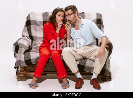 Ritratto di coppia, uomo e donna guardando la TV, film insieme isolato su sfondo bianco. Bere da una tazza Foto Stock