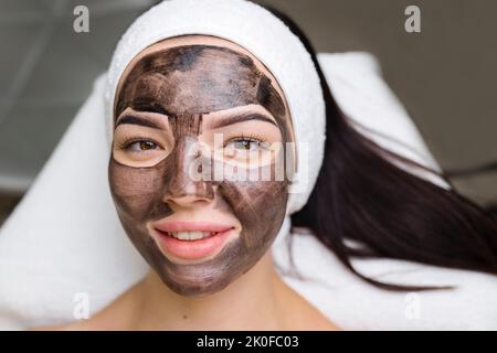 cosmetologo applicazione maschera nera sul viso bella donna indossare guanti neri, donna splendida in spa che hanno le procedure facciali Foto Stock