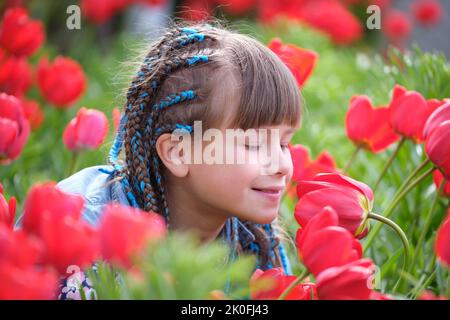 Ragazza felice bambino godendo dolce odore di tulipano rossi fiori in giardino d'estate Foto Stock