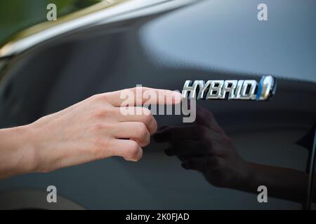 Mano umana che mostra il cartello dell'auto ibrida sul nuovo veicolo efficace Foto Stock