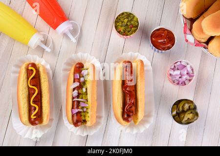 La vita ferma di un tavolo da picnic estivo con hot dog e condimenti. Tre franchi in cuccette con ketchup, senape, e gustare circondato da condimento Foto Stock