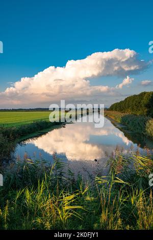 Dissipare la nuvola di tempesta si riflette nelle acque calme di un canale in una serena serata estiva Foto Stock