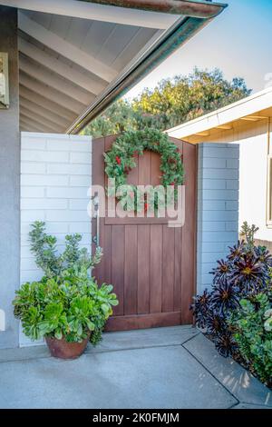 La Jolla, California - cancello unico in legno con corona e piante a lato della casa. Cancello a lato della casa a sinistra con dipinto di bianco Foto Stock