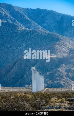 Palm Springs, California - fila diritta di turbine eoliche su una cespula. Mulini a vento contro la vista di un pendio secco di montagna sullo sfondo. Foto Stock