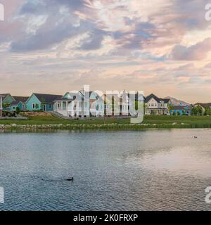 Nuvole Puffy Square al tramonto Vista panoramica del lago Oquirrh con acqua riflettente a Daybreak, Utah. Ci sono grandi edifici residenziali e montoni Foto Stock