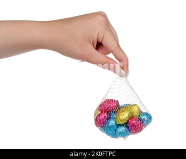 Giovane donna caucasica mano che tiene il sacchetto in rete con foglio colorato avvolto uova di Pasqua cioccolato, isolato su bianco. Foto Stock