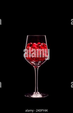 Bicchiere di vino ripieno di cristalli a forma di cuore rosso trasparente retroilluminati e isolati su sfondo nero. Concetto di amore e celebrazione. Spazio di copia. Foto Stock