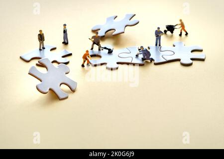 Squadra di minuscoli lavoratori in miniatura su pezzi di puzzle collegati jigsaw su carta giallo dorato. Primo piano su elementi puzzle bianchi. Foto Stock