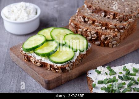 Fette di pane di segale con formaggio casereccio e cetrioli su sfondo grigio Foto Stock
