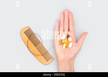 Ampolle cosmetiche con siero in mano femmina e vitamine per la crescita dei capelli, restauro capelli di bellezza. Pettine di legno con perdita di capelli su sfondo grigio. Foto Stock