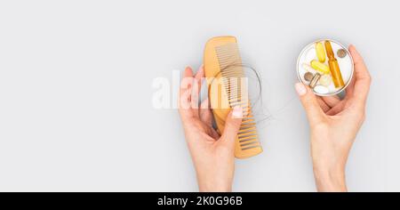 Ampolle cosmetiche con siero in mano femmina e vitamine per la crescita dei capelli, restauro capelli di bellezza. Pettine di legno con perdita di capelli su sfondo grigio. Foto Stock