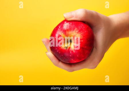Defocus femmina mano che tiene la mela rossa su sfondo giallo. Frutta e verdura biologica. Mani di coltivatori con le mele appena raccolte. Il male biblico. Foto Stock