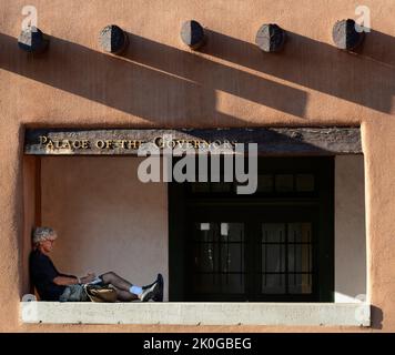 Un uomo scrive nel suo diario mentre si rilassa di fronte allo storico Palazzo dei Governatori a Santa Fe, New Mexico. Foto Stock