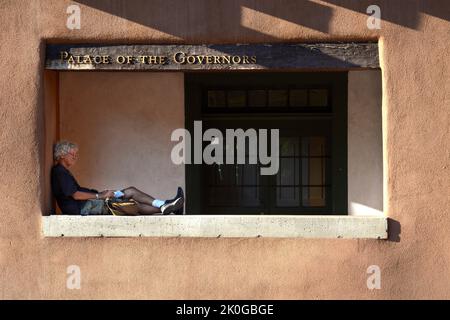 Un uomo scrive nel suo diario mentre si rilassa di fronte allo storico Palazzo dei Governatori a Santa Fe, New Mexico. Foto Stock