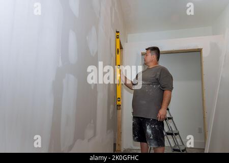 Prima di dipingere un muro di cartongesso, un dipendente controlla il livello del muro utilizzando un livello prima di dipingerlo Foto Stock