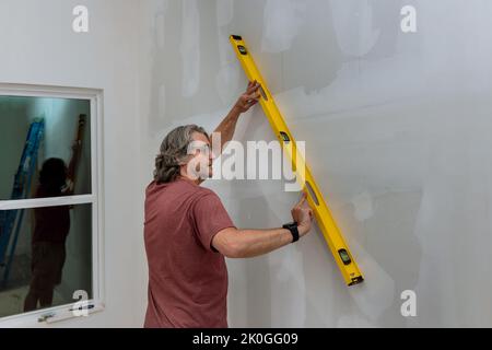 Un dipendente controlla il livello di un muro di cartongesso prima di eseguire la verniciatura utilizzando un livello per assicurarsi che i muri siano uguali Foto Stock