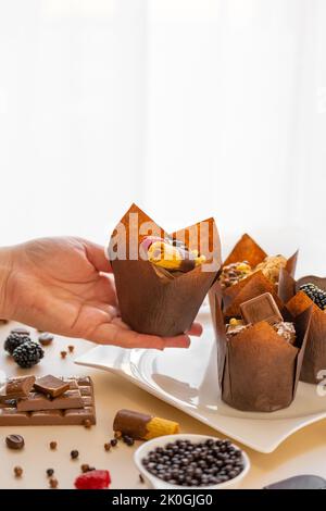 Muffin in mano sul tavolo con dolci e dolci. Dessert al cioccolato. Dolci assortiti. Dolci e dessert. Prodotti da forno e dessert Foto Stock
