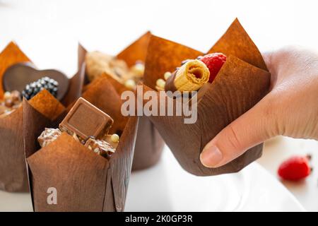 Chocolatemuffin in mano sul tavolo con dolci e dolci. Dessert al cioccolato. Dolci assortiti. Dolci e dessert. Prodotti da forno e dessert Foto Stock