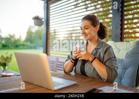 Felice giovane donna sta lavorando seduto sul patio in estate. Foto Stock