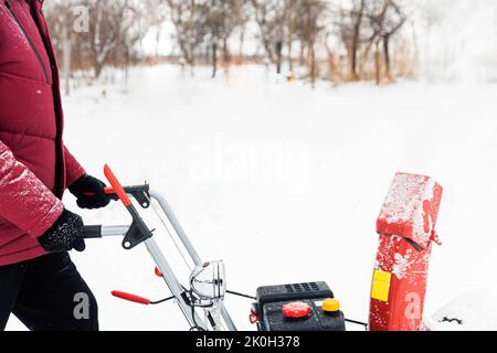 Particolare di soffiatore portatile di neve rossa alimentato a benzina in azione. Uomo all'aperto che usa una macchina spazzaneve dopo la tempesta di neve. Rimozione della neve, aiuto lanciatore in inverno. Ragazzo che soffia neve durante la Blizzard Foto Stock