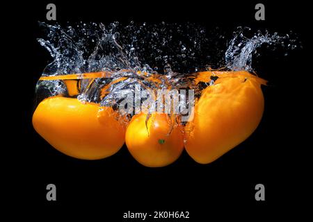 Pomodori freschi in pasta d'arancia caduti in acqua con spruzzi su fondo nero. Foto Stock