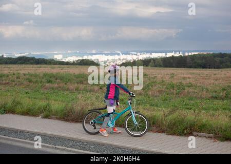 Una bambina sulla sua bicicletta e ha smesso di guardare il paesaggio thecityscape di fronte a lei. Le nuvole sono blu grigio e minacciose. Indossa un casco Foto Stock