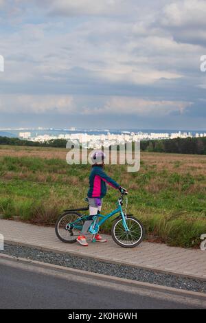 Una bambina sulla sua bicicletta e ha smesso di guardare il paesaggio thecityscape di fronte a lei. Le nuvole sono blu grigio e minacciose. Indossa un casco Foto Stock