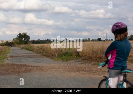 Una bambina sulla sua bicicletta e si fermò a guardare il paesaggio di fronte a lei. Le nuvole sono blu grigio e minacciose. Il bambino in aiuto è tornato Foto Stock