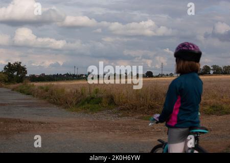 Una bambina sulla sua bicicletta e si fermò a guardare il paesaggio di fronte a lei. Le nuvole sono blu grigio e minacciose. Indossa un casco Foto Stock