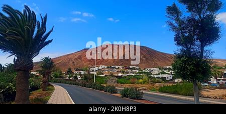 Una bella vista di una strada con palme e case con montagna sullo sfondo Foto Stock