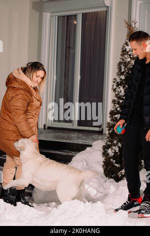 L'uomo in piedi con una palla per giocare con il suo cane fuori e il cane bianco corse a donna proprietario vuole giocare con lei. Foto Stock