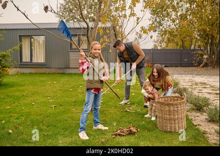 Tutta la famiglia pulisce il cortile in autunno Foto Stock