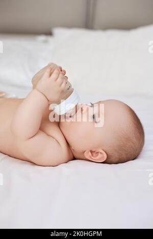 la bambina si trova nel letto e beve acqua da una bottiglia Foto Stock