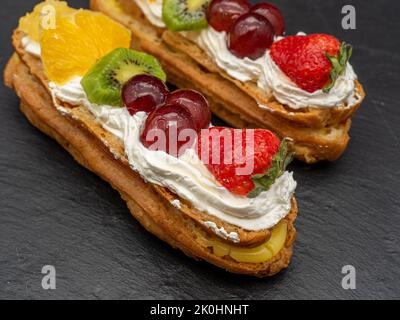 Un primo piano di due eclair con panna montata, frutti di bosco e frutta Foto Stock