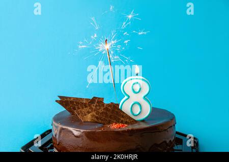 Numero 8 candela di compleanno bruciante e scintillante con scintille volare sulla torta. Concetto di celebrazione di otto anni di anniversario. Molto spazio di copia su blu. Foto Stock